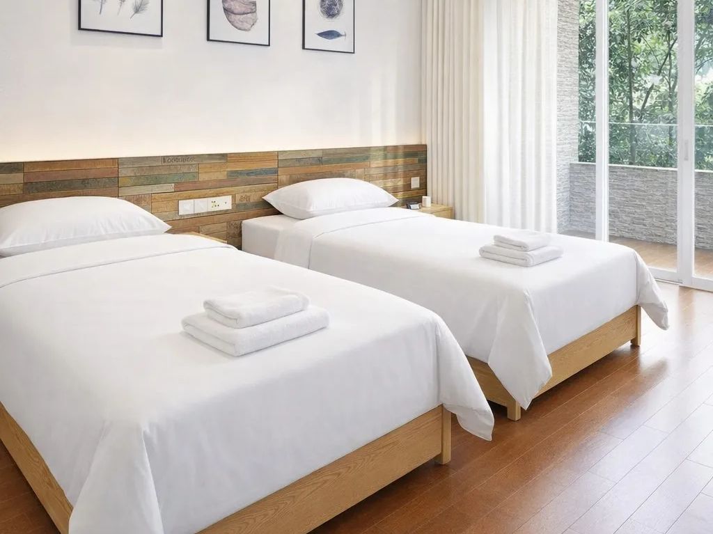 A hotel room with two beds, a wooden headboard, and a view of greenery through large windows.