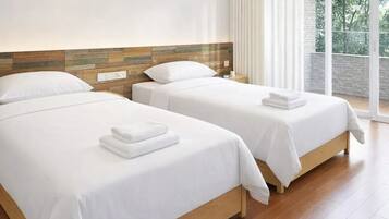 A hotel room with two beds, a wooden headboard, and a view of greenery through large windows.