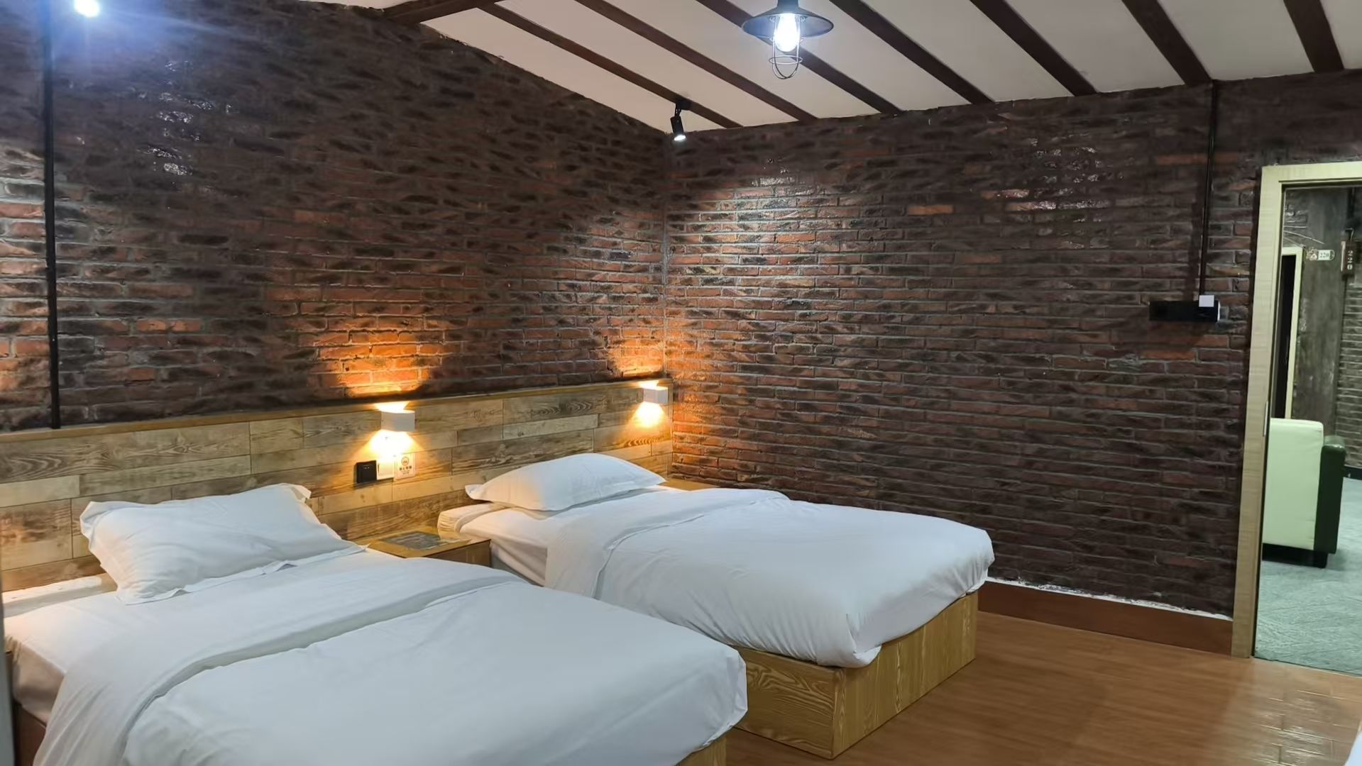 A room with two beds, wooden headboards, and brick walls.