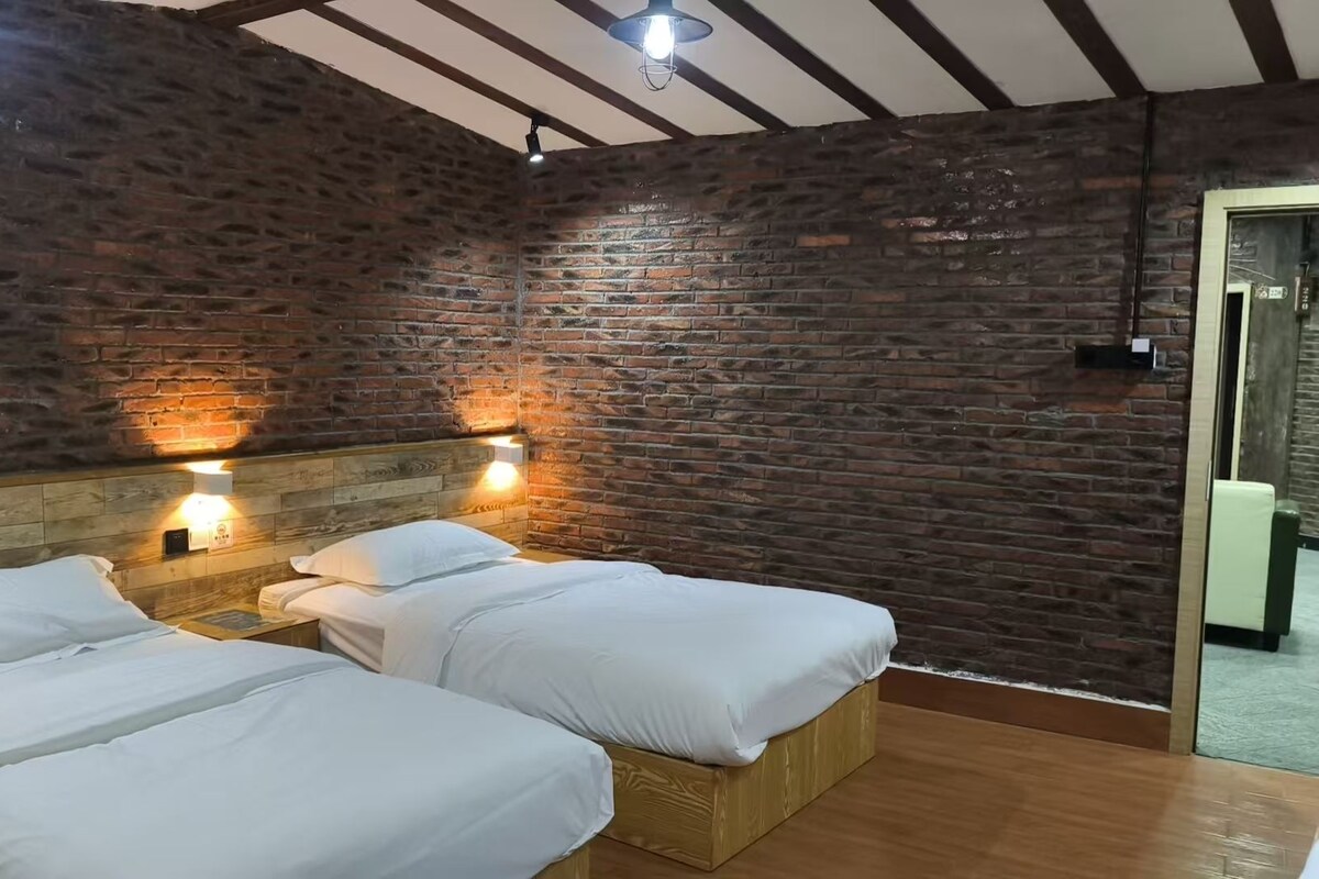 A room with two beds, wooden headboards, and brick walls.