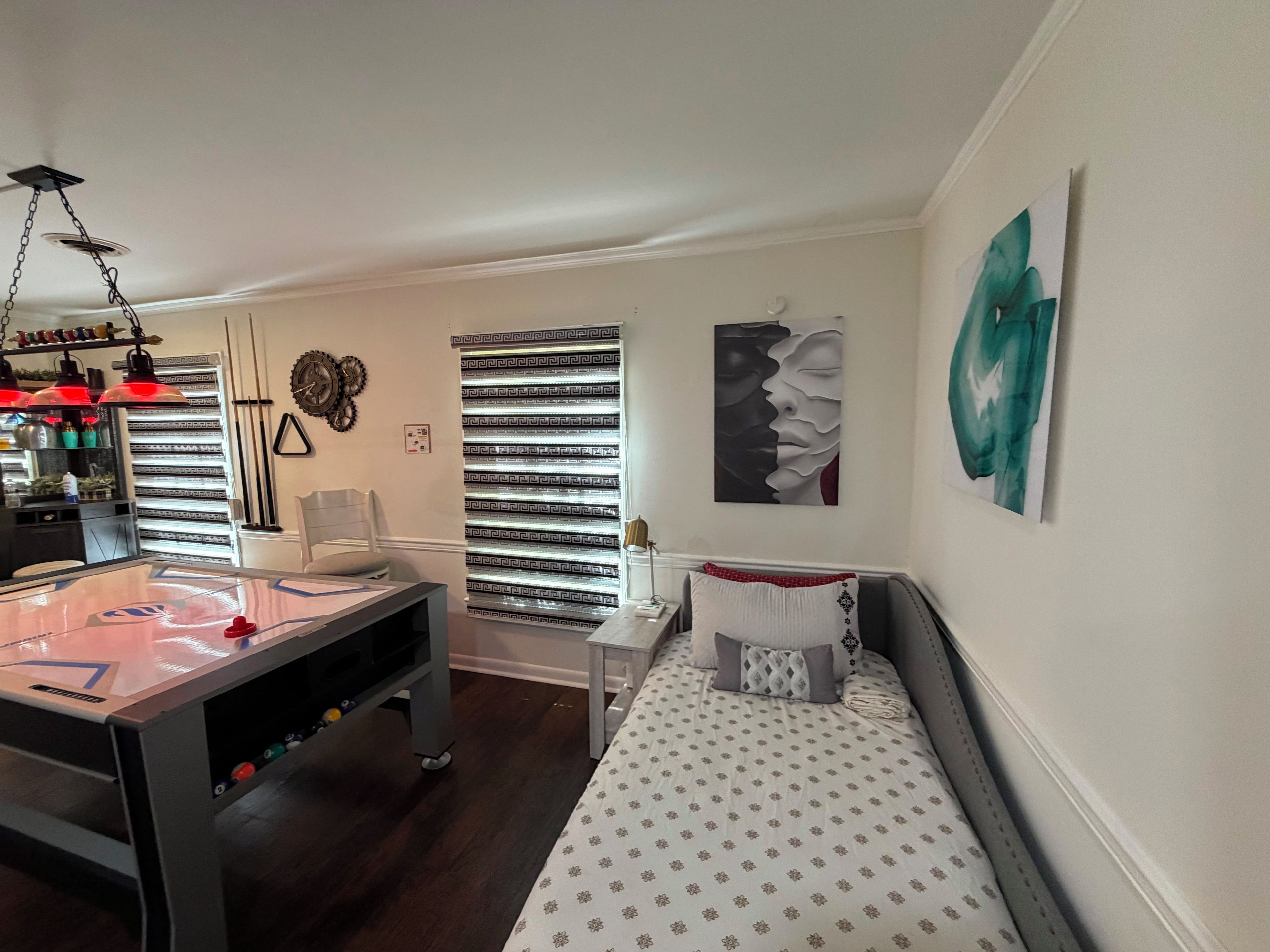 Een kamer met een eettafel, een bank, een kunstwerk aan de muur en een raam met decoratieve jaloezieën.