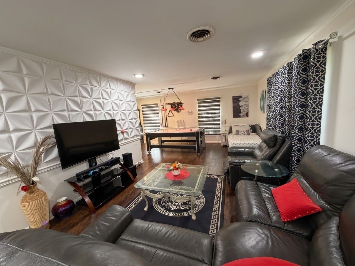 A modern living room with a leather sofa, a glass coffee table, a flat-screen TV, and a patterned wall.