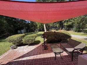A patio with a red shade sail, a metal table, and two chairs. - Modern Gamer”s Haven - Relax & Play (Jackson)