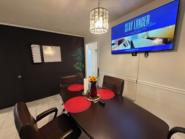 Een eethoek met een donker houten tafel, rode placemats en twee bruine stoelen. Een televisie aan de muur toont een advertentie.