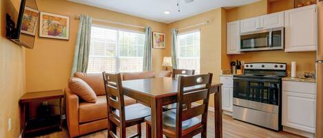 A modern kitchen with a dining area, wooden chairs, a sofa, and a ceiling fan.