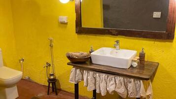 A bathroom with a yellow wall, a white sink, a mirror, a toilet, and a shower.