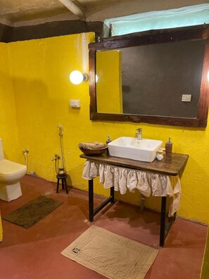 Une salle de bain avec un mur jaune, un lavabo blanc, un miroir, des toilettes et une douche.