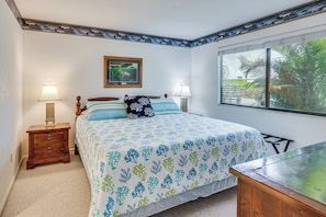 A bedroom with a bed, two bedside tables, a nightstand, a window with a view of greenery, and a framed picture on the wall.