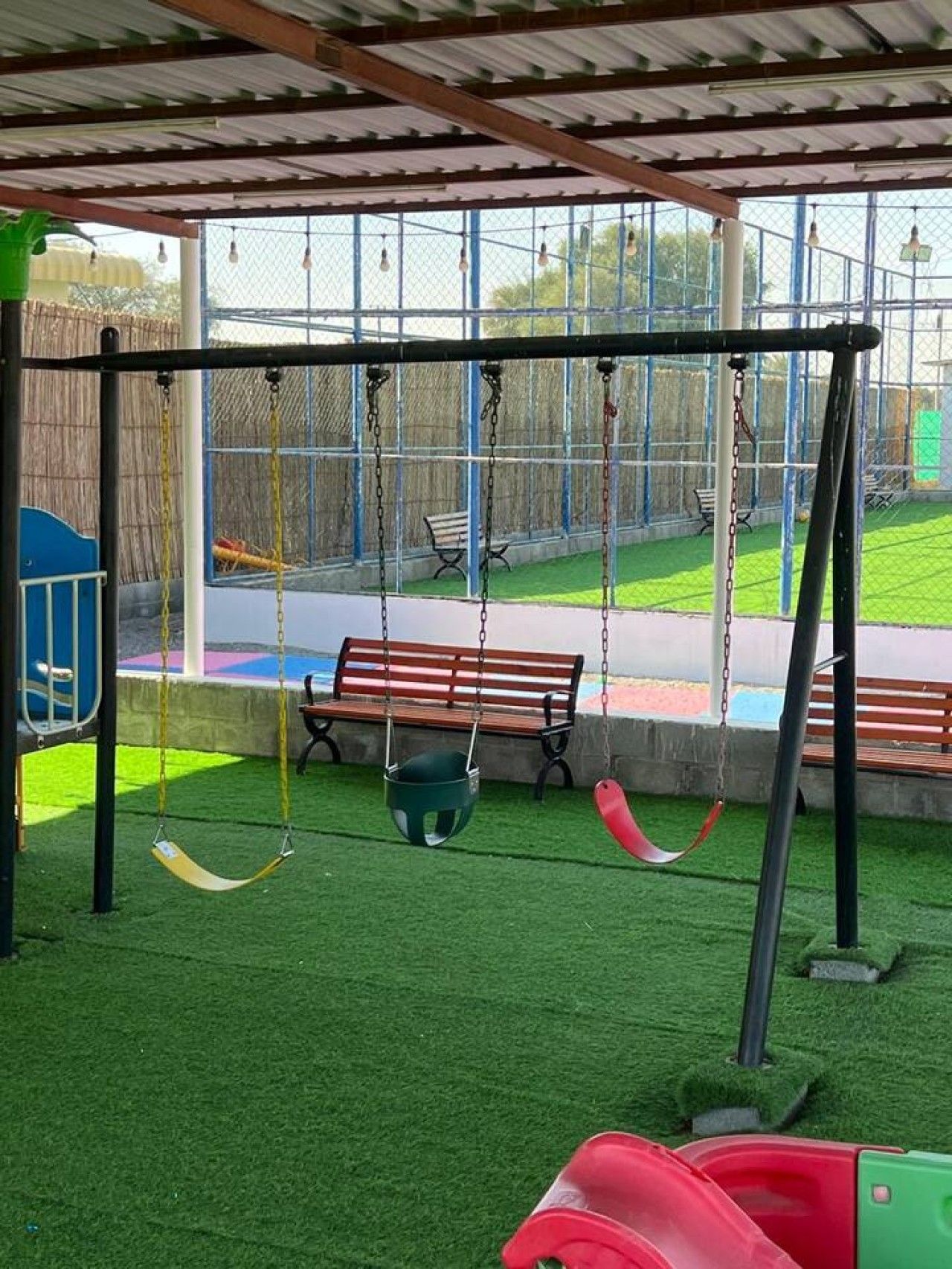 Un parque infantil con columpios, un tobogán y césped artificial.