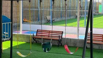Un parque infantil con columpios, un tobogán y césped artificial.