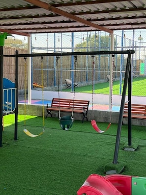 A playground with swings, a slide, and artificial grass.