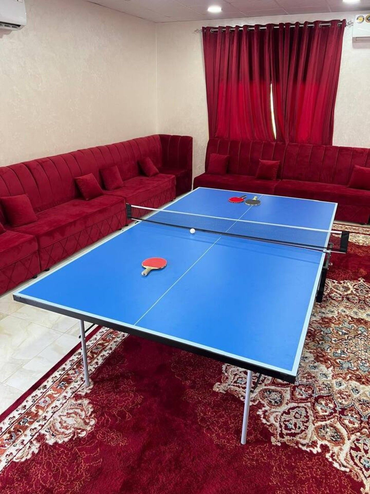 Una habitación con dos mesas de ping pong, sofás rojos y una alfombra estampada.