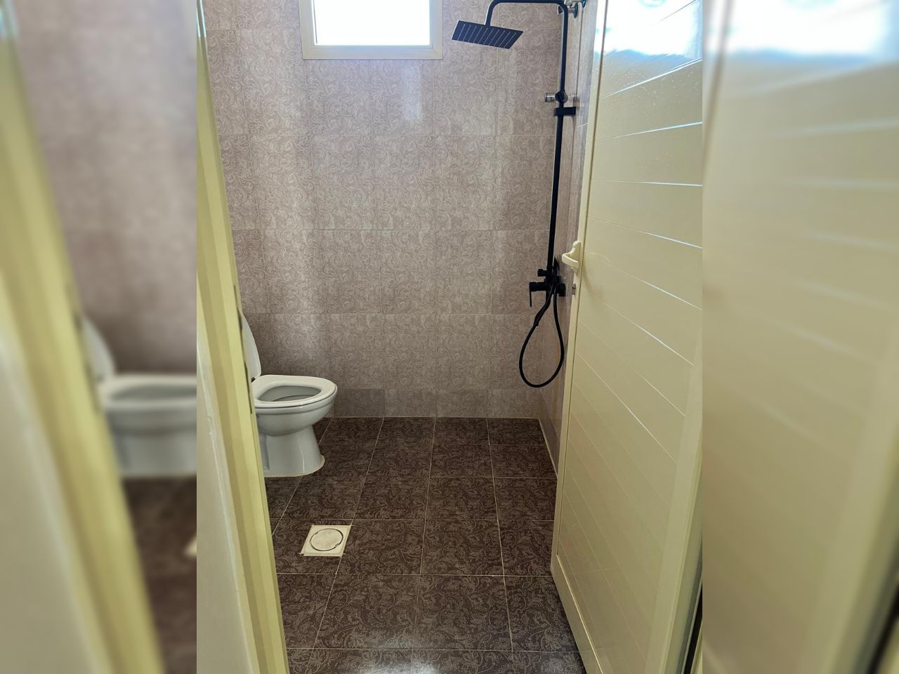 Un baño con inodoro, ducha y baldosas estampadas.