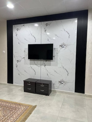 A room with a television mounted on a marble wall, a black cabinet below, and a patterned rug on the floor.