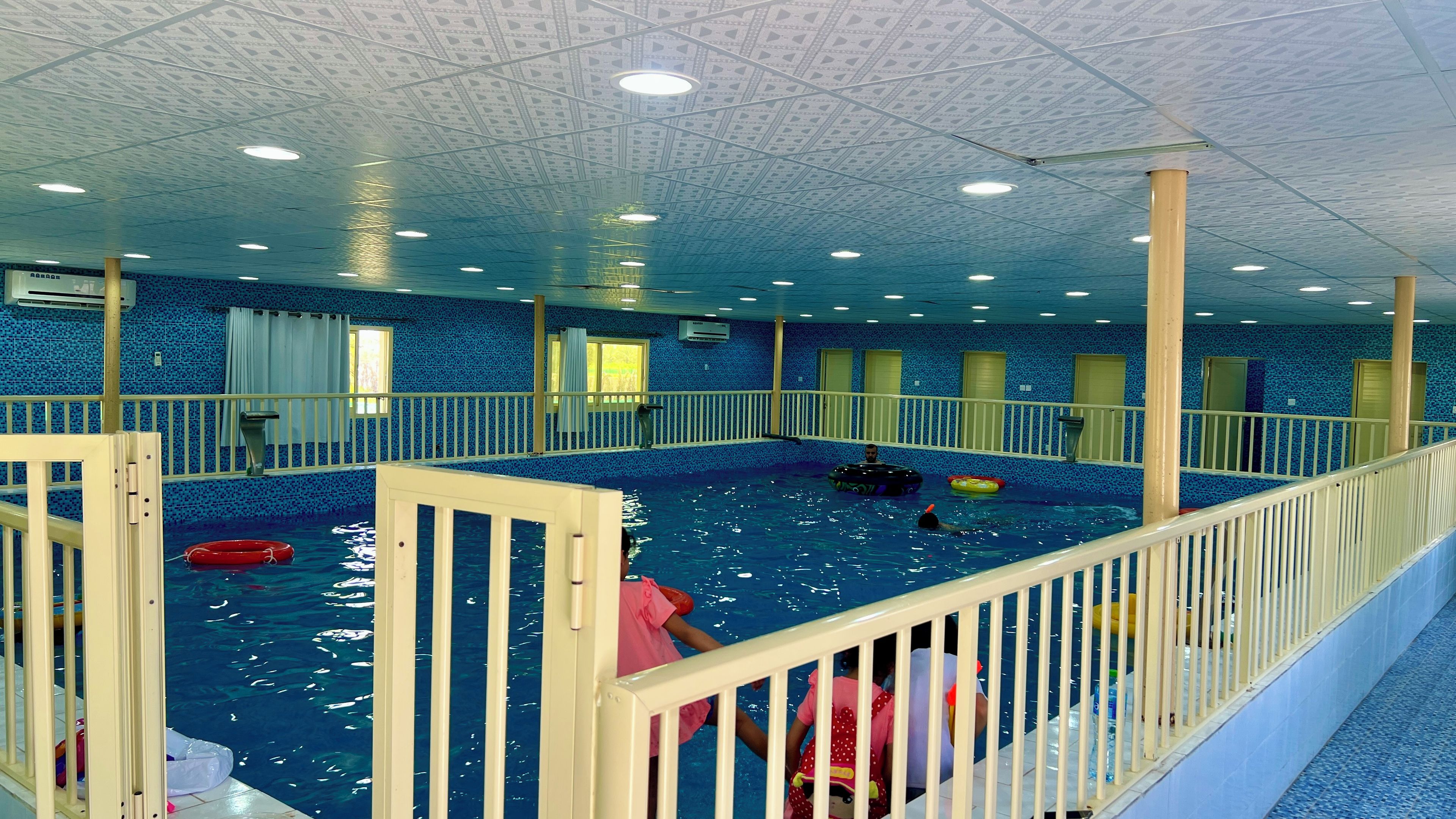 An indoor swimming pool with a tiled floor, a wooden deck, and a ceiling with a geometric pattern.