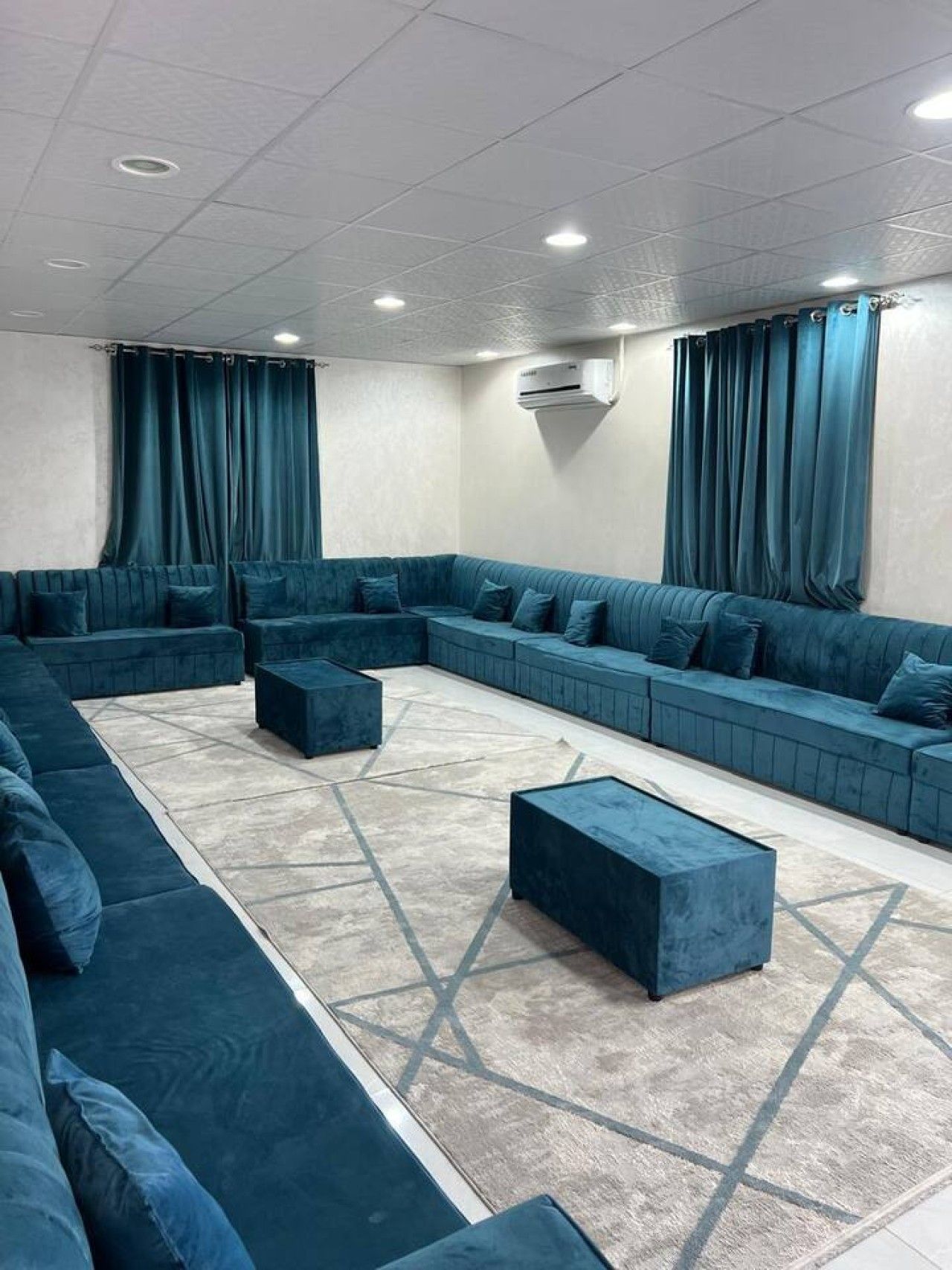 A modern lounge area with a sectional sofa, ottomans, and a patterned rug.
