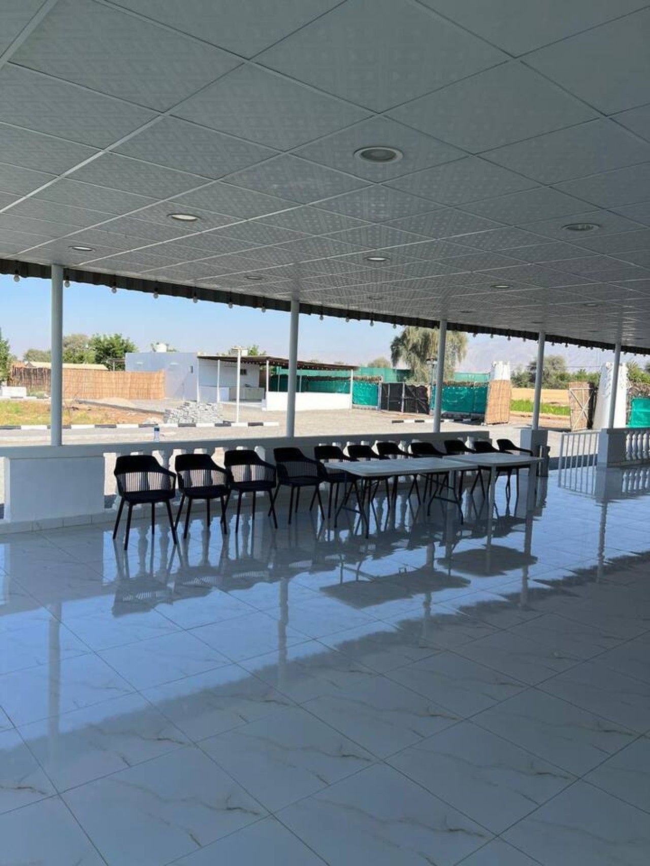 An indoor covered area with a tiled floor, several tables and chairs, and a view of the outside.