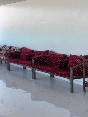Una fila de sofás rojos con cojines estampados frente a una pared lisa, con piso de baldosas.