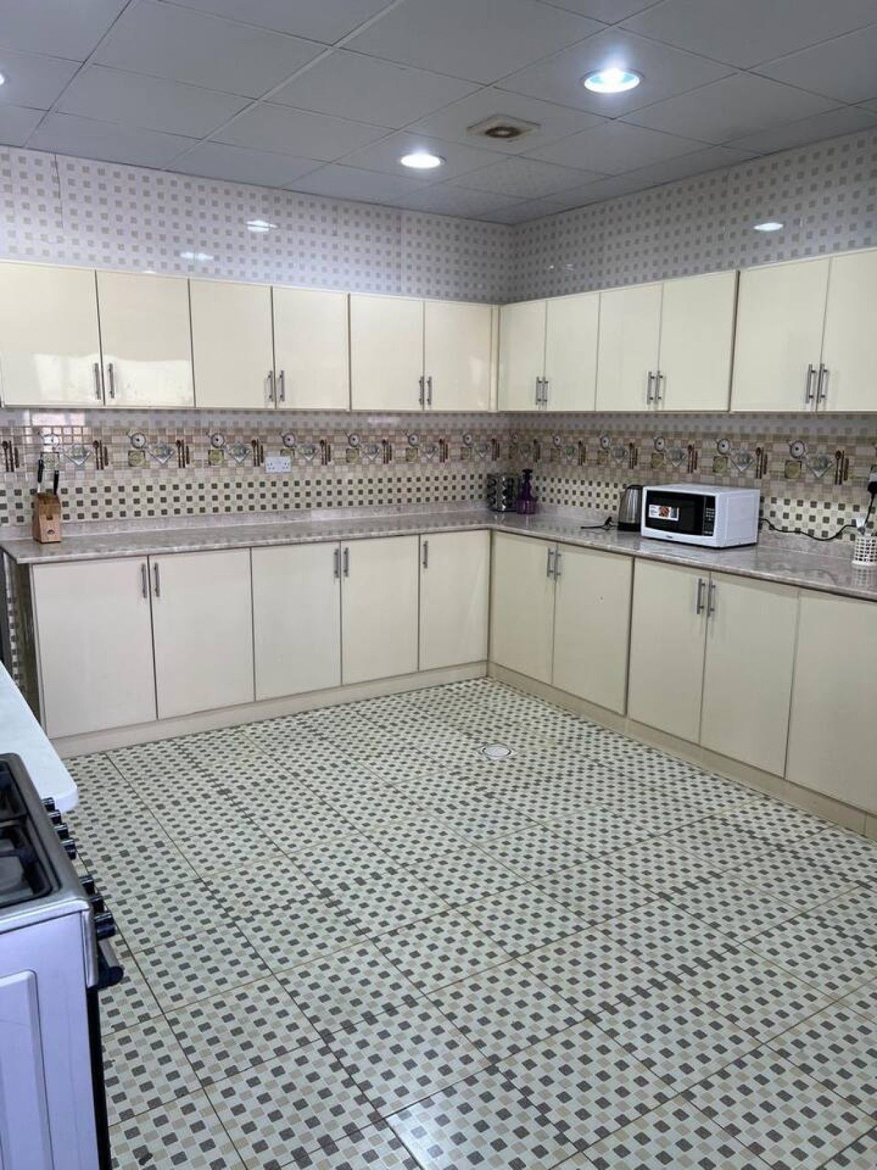 Una cocina con armarios blancos, un microondas y un suelo estampado.