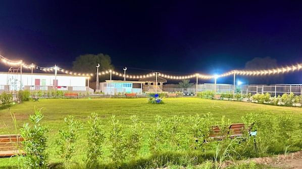 Un espace extérieur doté d’une pelouse, de bancs et de guirlandes lumineuses.