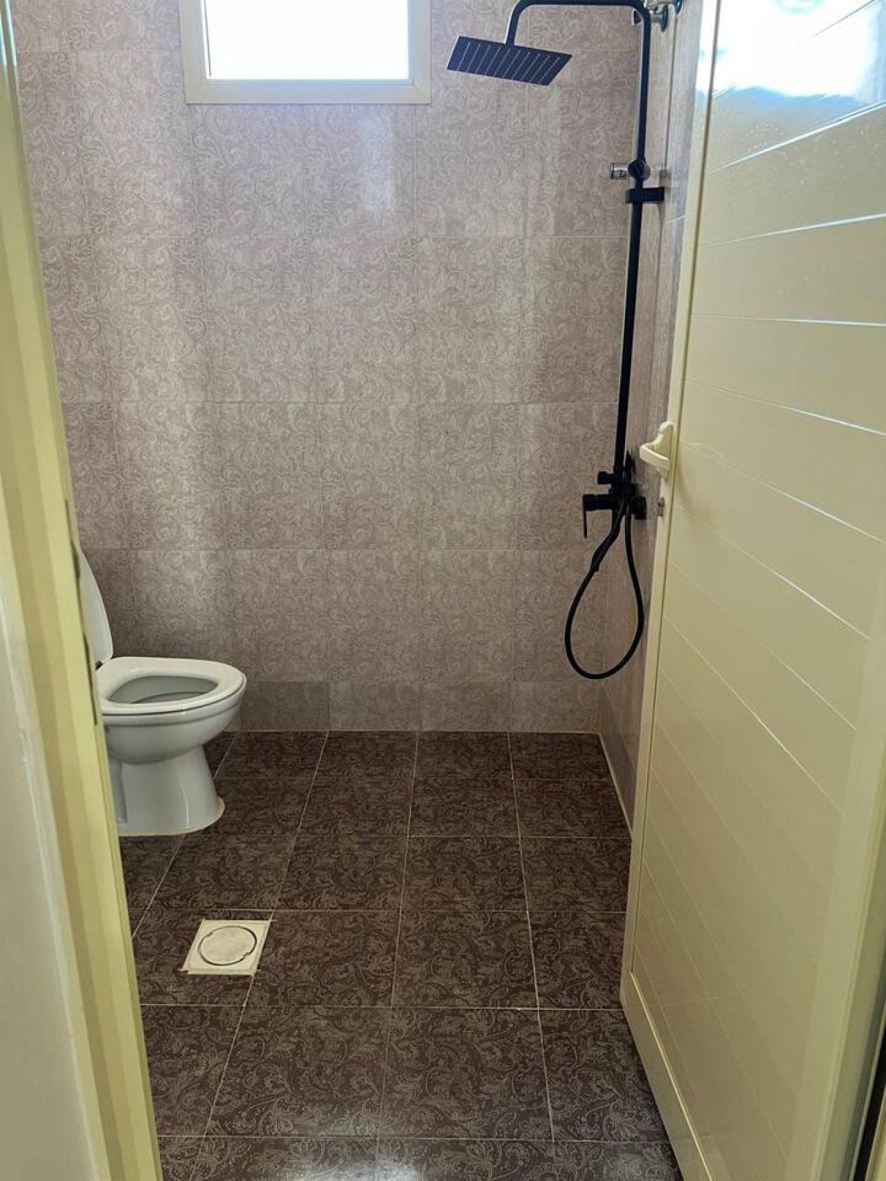 A bathroom with a toilet, shower, and a window.