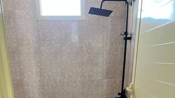 A bathroom with a toilet, shower, and a window.