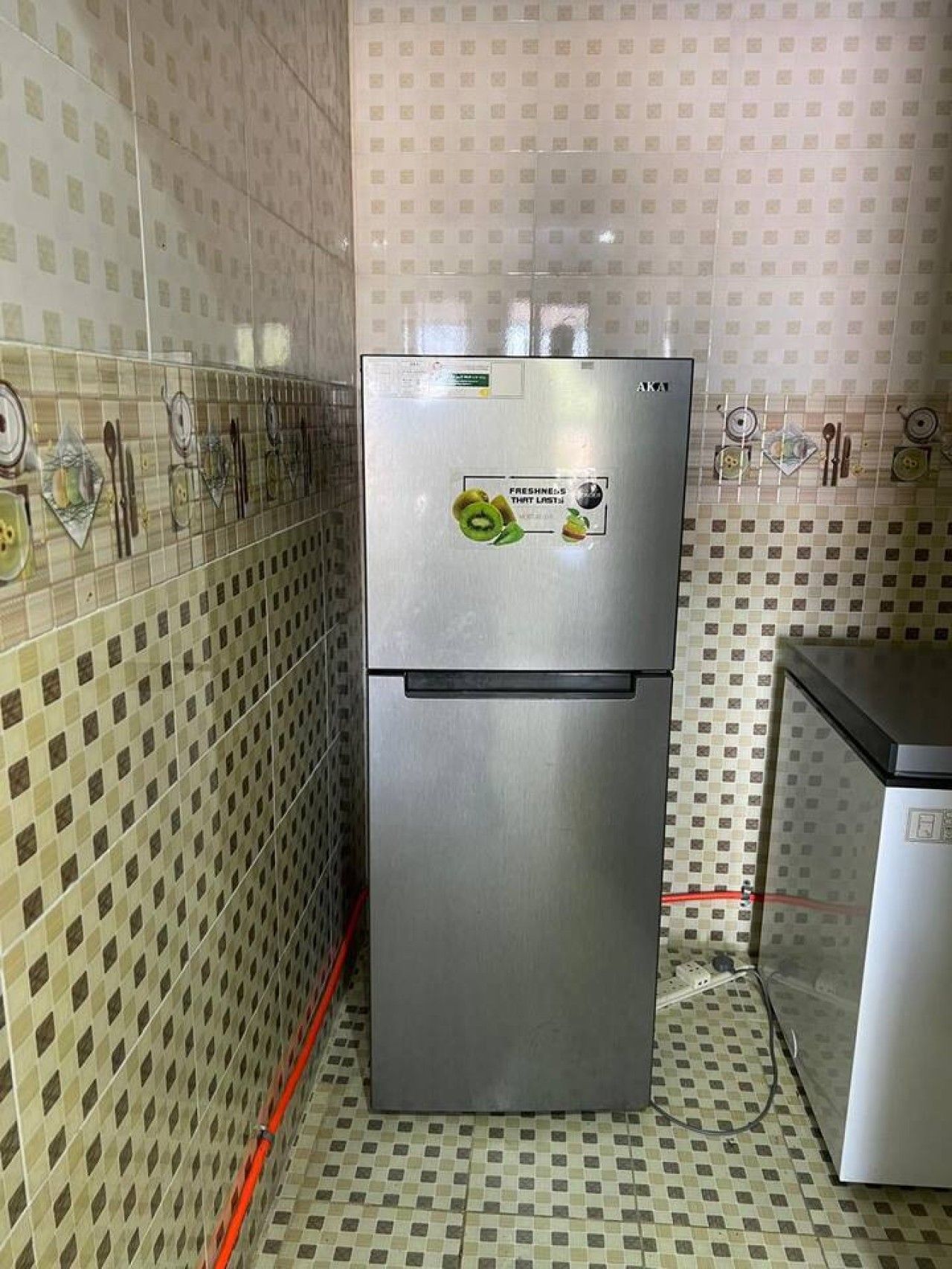 A kitchen with a stainless steel refrigerator, tiled walls, and a tiled floor.