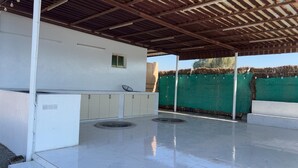 Un espace extérieur abrité, doté d’un comptoir blanc, d’une petite fenêtre et d’une clôture verte en arrière-plan.
