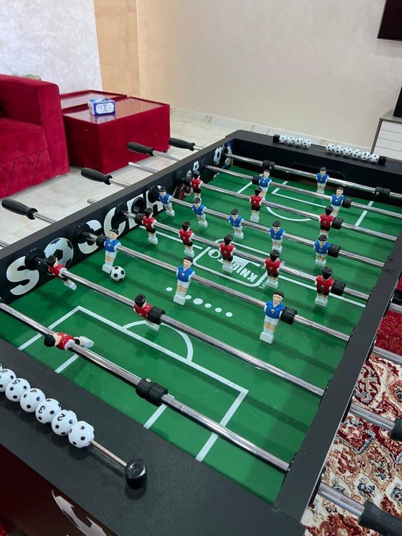 Una mesa de fútbol de mesa con superficie verde y dos equipos de jugadores.