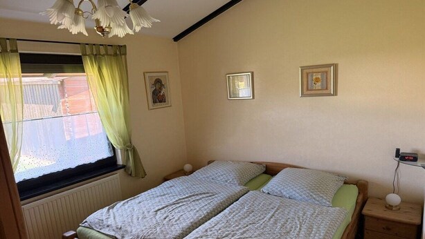 Una habitació amb dos llits, una finestra amb cortines, un rellotge penjat a la paret i una petita taula de nit amb una làmpada.