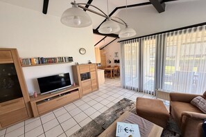A modern living room with a flat-screen TV, wooden furniture, and a dining area in the background. - Dike Break J3||Eckwarderhörne (Eckwarderhörne)