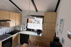 A compact kitchen with wooden cabinets, a black countertop, and a window with a view of a house. - Dike Break J3||Eckwarderhörne (Eckwarderhörne)