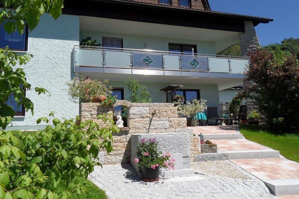 A two-story building with a balcony, stone steps, and potted plants.