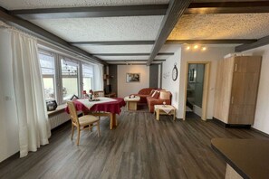 A room with a dining table, chairs, a sofa, a small table with a lamp, and a cabinet.