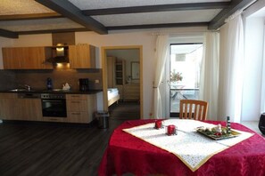 A compact kitchen with modern appliances, a dining area with a red tablecloth, and a view through a doorway to an outdoor balcony.