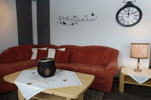 A red sofa with a white throw blanket, a small wooden table with a white tablecloth, a black candle holder, and a wall clock.