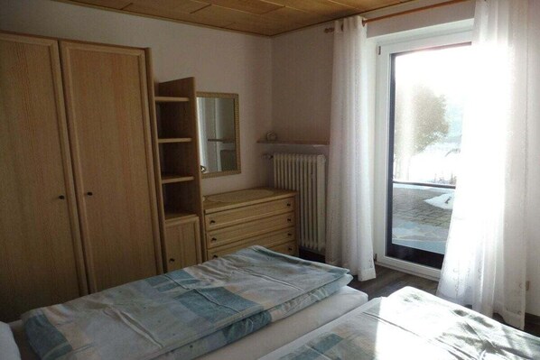 A bedroom with a bed, a dresser, a mirror, and a window with curtains. - Holiday apartment in Fichtelberg with Wi-Fi (Fichtelberg)