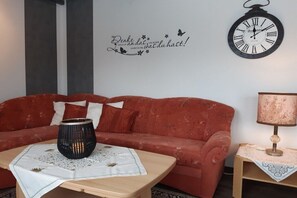 A room with a red sofa, a wooden coffee table, a wall clock, and a decorative sign.