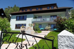 A two-story house with a balcony, a stone staircase, and a well-maintained lawn.