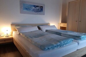 A double bed with a headboard, a bedside table with a lamp, a wardrobe, and a framed picture on the wall.