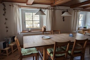 Une table à manger en bois avec des chaises, une fenêtre avec des rideaux et une lampe suspendue.