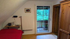 Une chambre avec un couvre-lit rouge, un radiateur, une porte en bois et une fenêtre donnant sur un balcon.