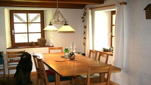 Un comedor con mesa de madera, sillas y un perro sentado junto a la ventana.