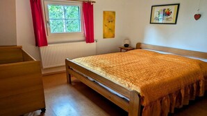 Un dormitorio con cama de madera, radiador, ventana con cortinas rojas y una mesita de noche pequeña.