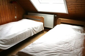 Une chambre avec deux lits en bois, un plafond en pente et un puits de lumière.