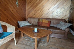 Een gezellige kamer met een houten plafond, een bruine leren bank, een rieten stoel en een houten salontafel.