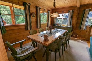 Interior d'una cabana de fusta amb taula de dinar, cadires i un osset de peluix damunt la taula.