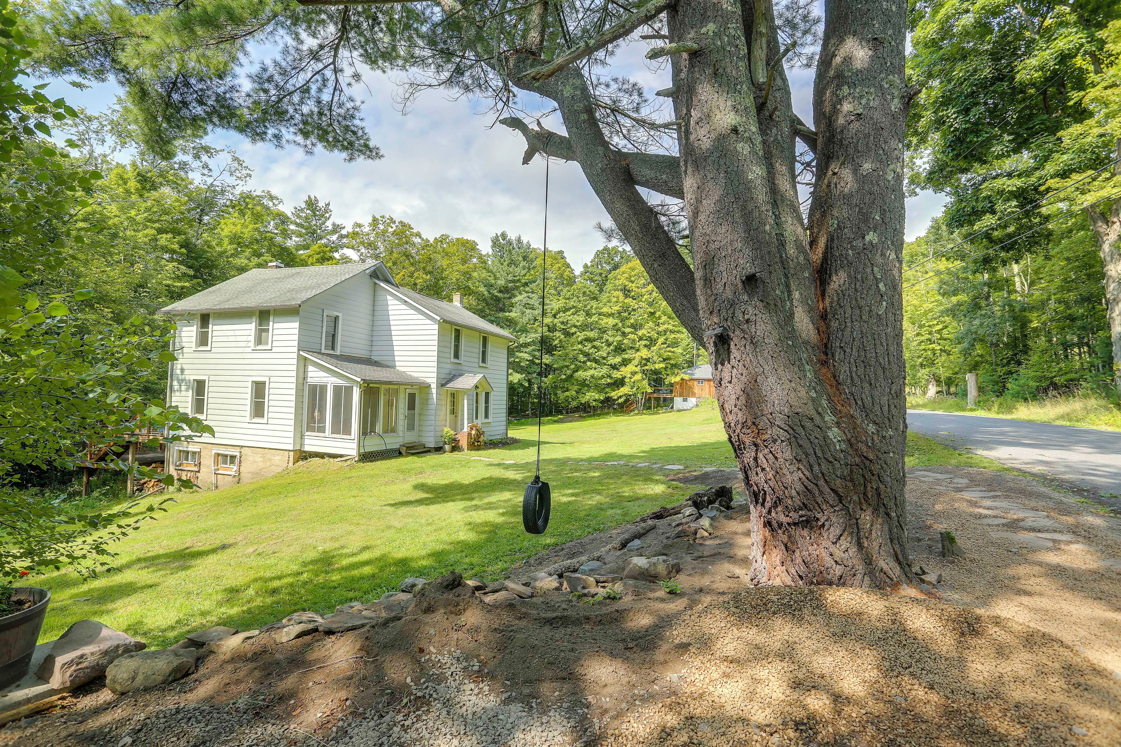 A two-story house with a porch and a swing hanging from a large tree.