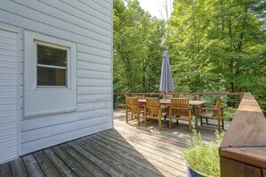 Eine Terrasse mit Holztisch und -stühlen, einem Fenster und Blick auf ein bewaldetes Gebiet.