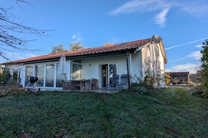 A single-story house with a tiled roof, a glass door entrance, and a patio area with outdoor furniture. - Michaela holiday apartment (Heiligenberg)